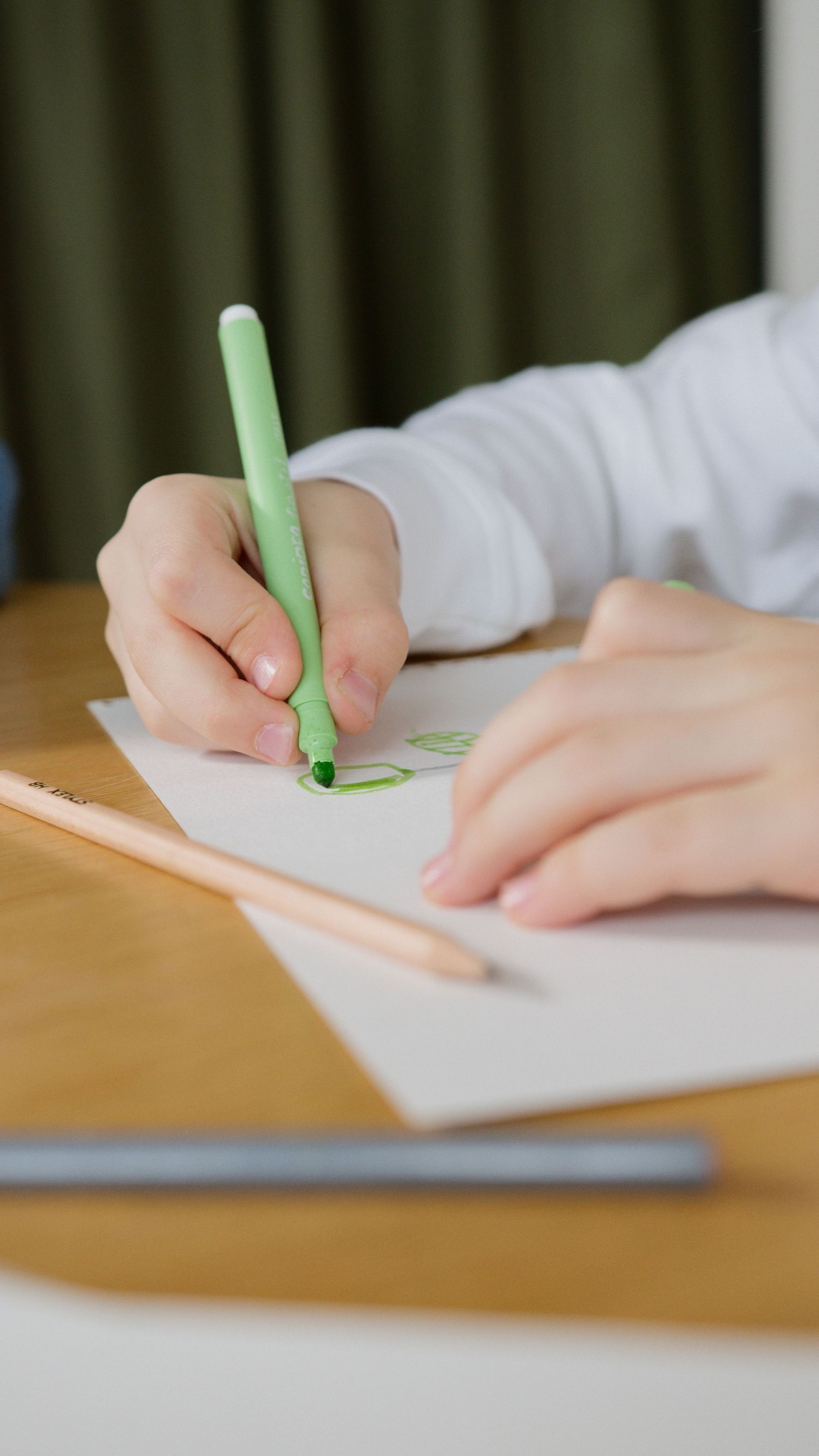 Close-up of a child drawing with a green pen, capturing creativity in education.